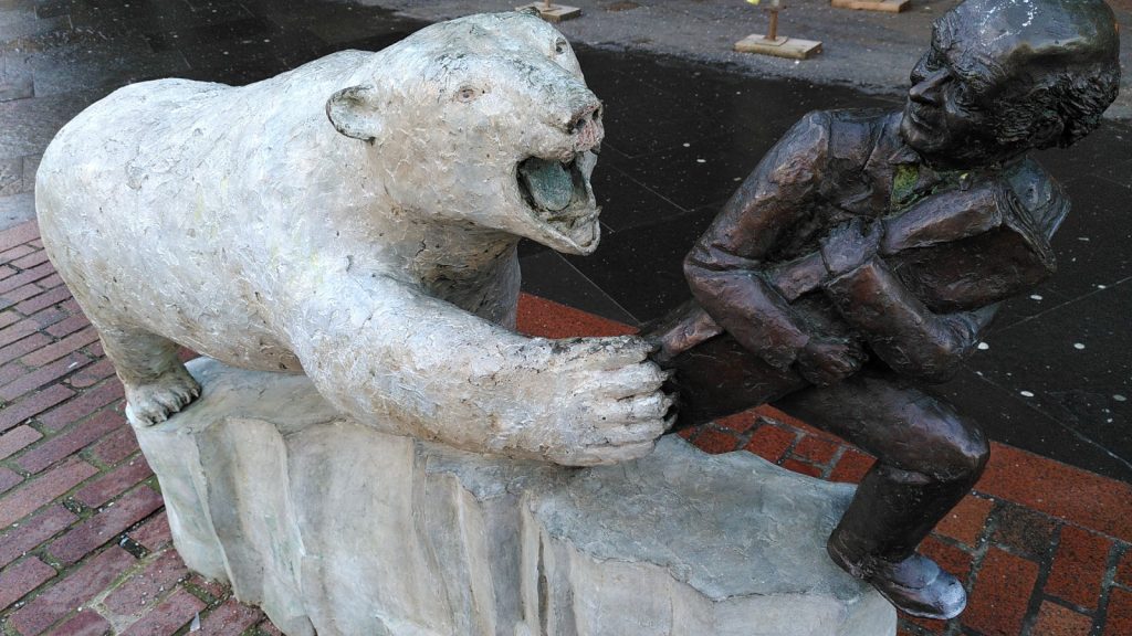 Statue of a polar bear chasing a man carrying a roll of cloth