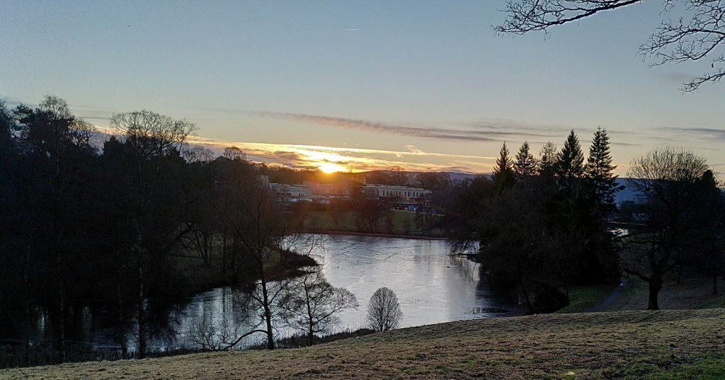Sunsetting over hills beyond a small lake in the grounds of Stirling University