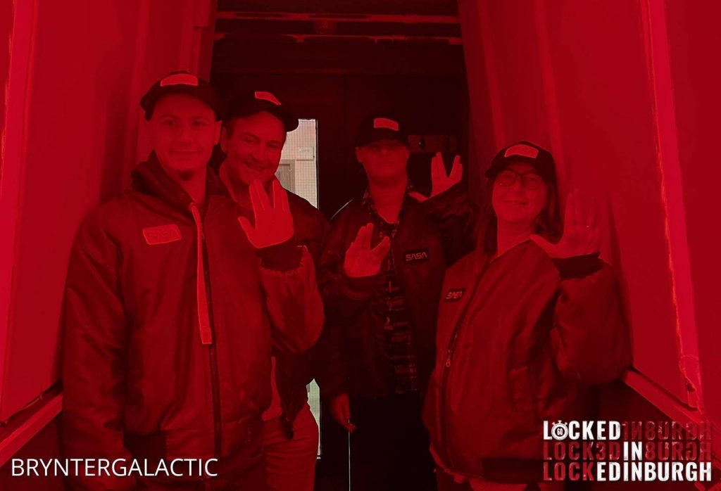 Four space cadets in jackets and caps in a red-lit hexagonal tunnel