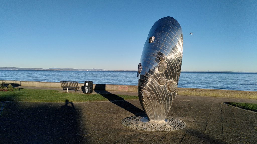 Silvery sculpture of giant mussel with blue sea and sky behind