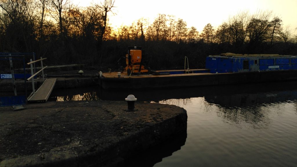 Fenced off upper lock with working boat moored upstream in evening light.