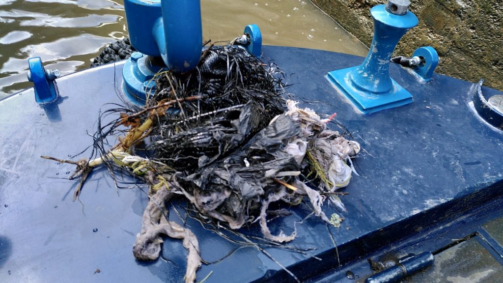 A mix of plastic, cloth and plant material sits in an untidy pile on the deck next in front of the tiller.