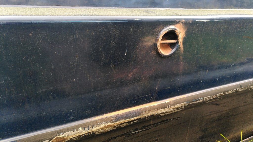 The side of a narrowboat  with a fitting for attaching a fender. The forward part has a splash of brick dust. There is also brick dust on a ledge below.