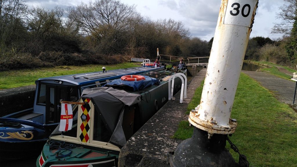 Two narrowboats side-by-side descending in a double lock. In the foreground is a white painted pillar - part of the lock mechanism.