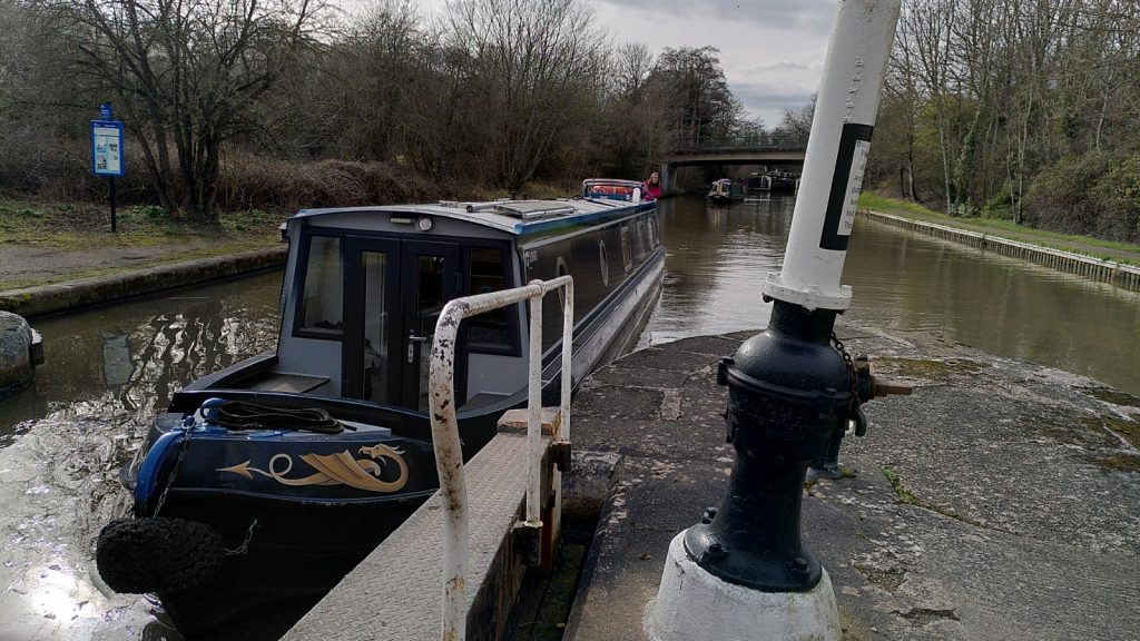 Bartimaeus entering the bottom lock. In the foreground, is an open lock gate and a white painted column. Further down the canal, another boat is following.