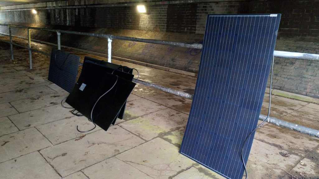 Solar panels leaning on a fence under a concrete bridge