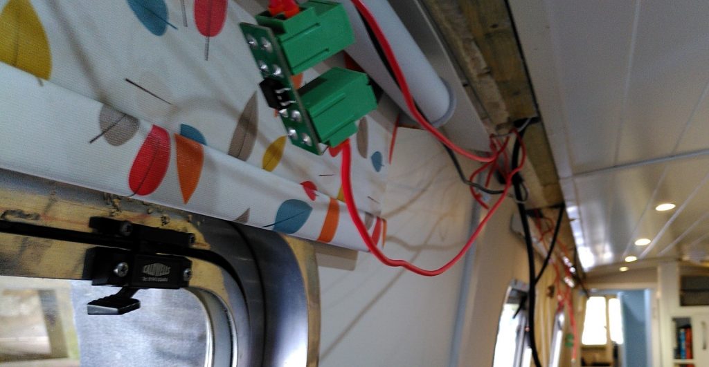 Narrowboat interior with cables dangling from the roof. In the foreground is a piece of electronic equipment with two green connectors.