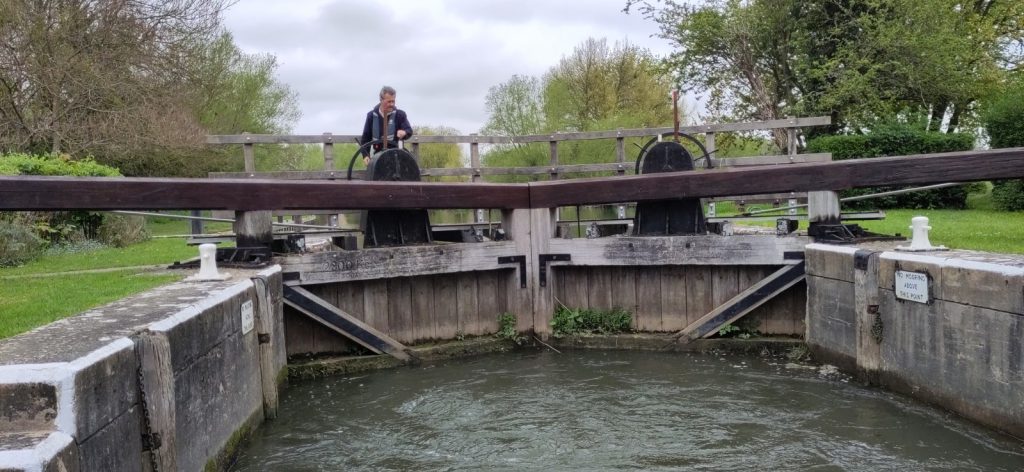 A large pair of lock gates viewed from inside the lock.  On top of each gate is a wheel similar to that used to steer a boat.  A man is turning one of them to operate the paddles.