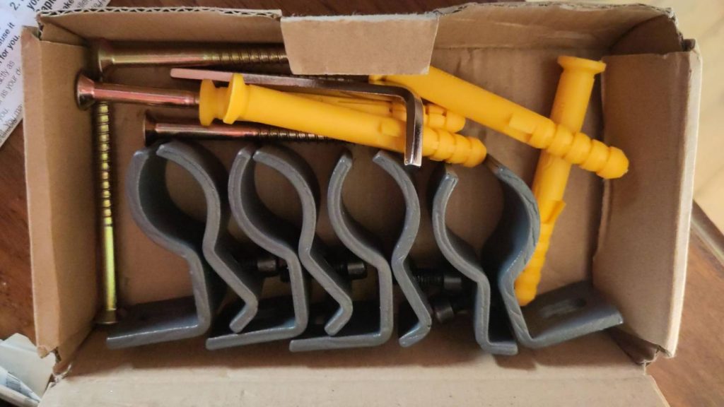 Cardboard box containing a set of four radiator brackets.  They are designed to clamp on to the tubes at the back of the radiator.  The box also contains some massive screws and plugs.