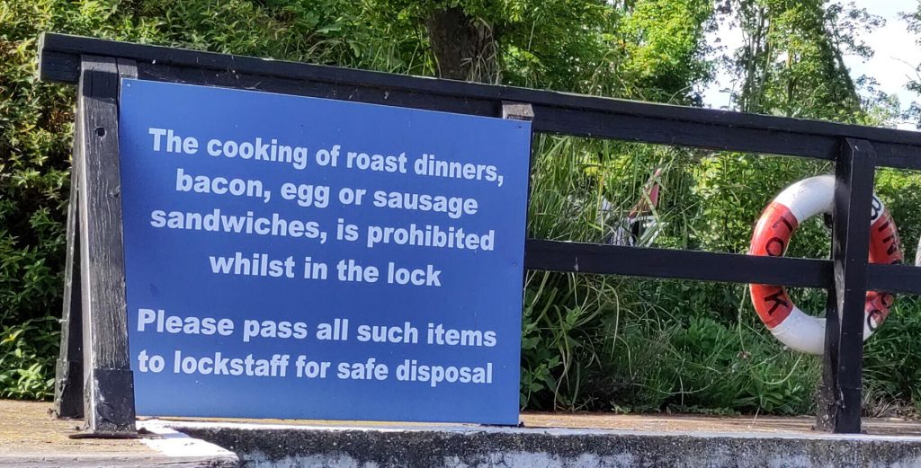 Large blue sign at the side of a lock. The text says: "The cooking of roast dinners, bacon, egg or sausage sandwiches, is prohibited whilst in the lock. Pleas pass all such items to lockstaff for safe disposal"