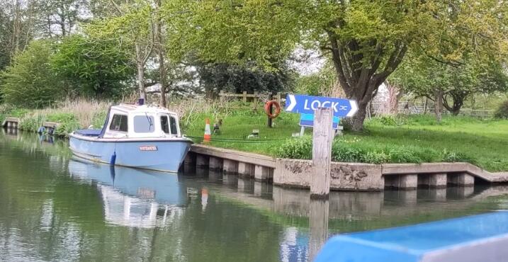 A sign on the side of the river shows the way to the lock.  Moored alongside is a small boat with a blue light on top.