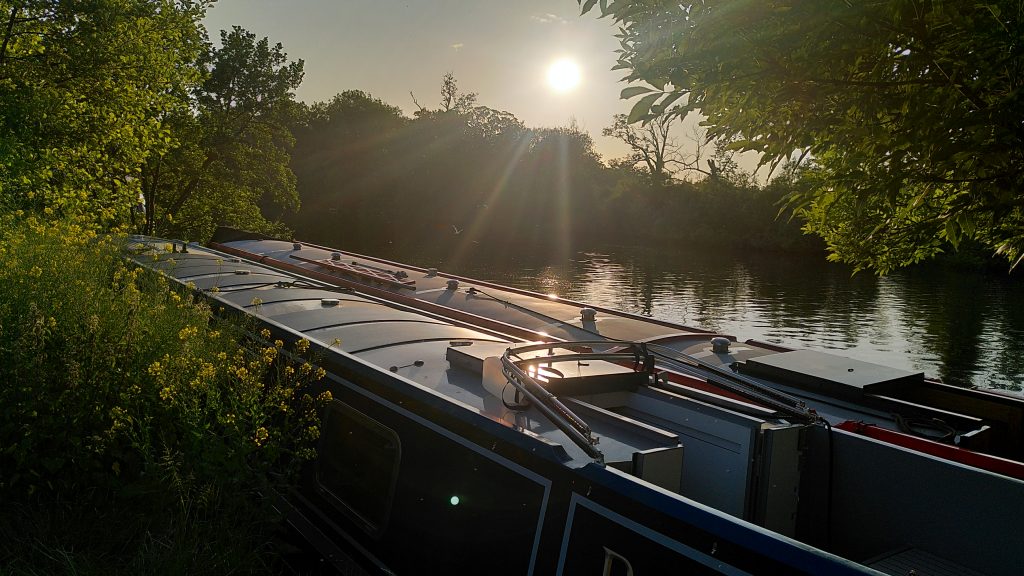 Two narrowboats moored side-by-side.  The sun is low in the sky over the trees on the opposite bank of the river.