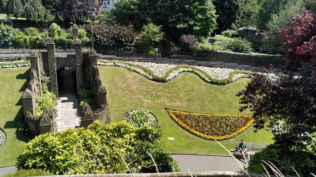 Castle Gardens with a path running through a stone turreted path.  The flower beds are arranged in intricate patterns and full of colour.