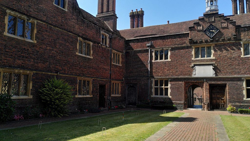 View in to a grassed courtyard, one side of which is set up as a croquet lawn. The brick and stone buildings are over four hundred year old.