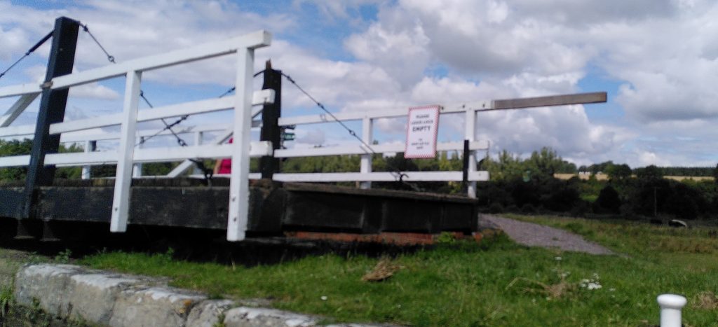 A swing bridge over a lock.  The bridge has a sign on it saying "Please leave lock empty to keep cattle safe".