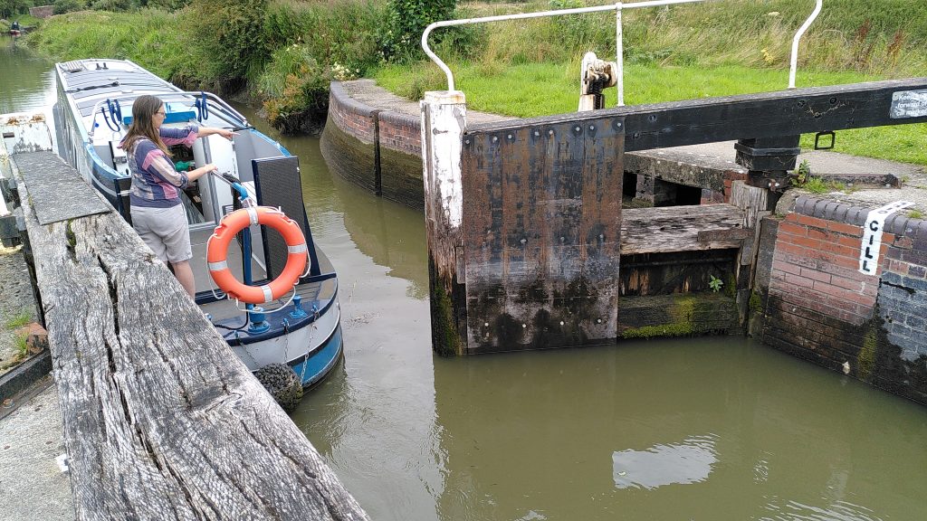 Narrowboat leaving through the top gate of a lock.  Damp marks around the edge of the lock and nearby canal show that the water level is at least two feet lower than it had been earlier.