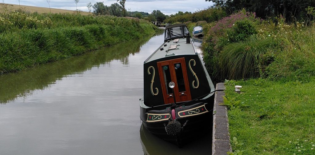 A narrowboat moored at the side of a canal. The boat is listing away from the bank where it has rested on the bottom as the canal has drained away.