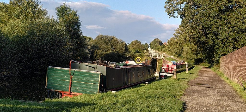 A view up the main Caen Hill Lock Flight.  The locks march up the hill in an even line towards a vanishing point.  In the foreground are boats waiting to enter the flight.