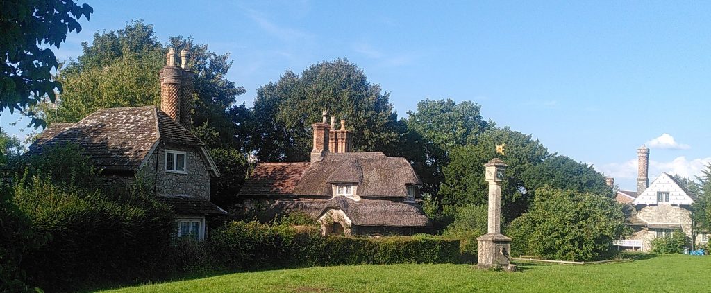 Cottages at Blaise Hamlet along the edge of the green.  In the green is a tower with a sundial.  Each of the three cottages visible is a a different shape with elaborate but distinctive chimneys.