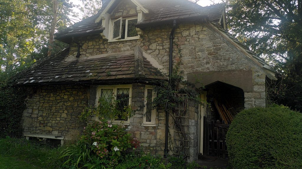 Stone cottage at Blaise Hamlet.  There is one bay window downstairs with another window above it.  The roof starts to slope in above the ground floor giving the building an almost pyramidal look.