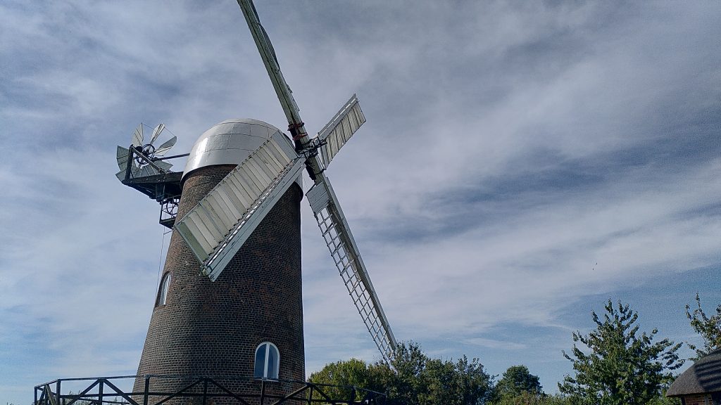 Wilton windmill.  The brick buiding has a shiy white metal domed cap.  The sails are stopped diagonally.