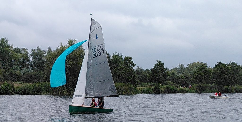 Small sailing boat with bright blue spinnaker.  Two crew members can be seen on the boat.