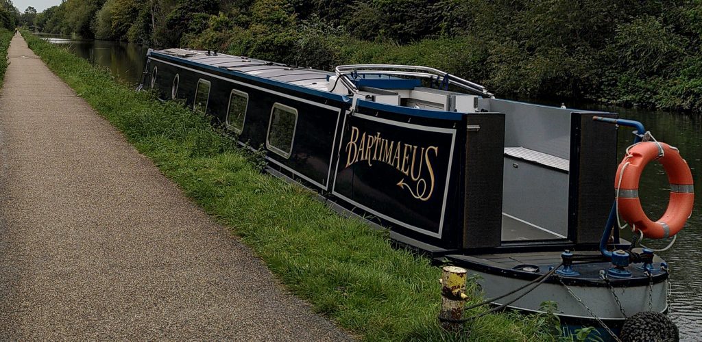 Narrowboat moored against a towpath.  The canal stretches ahead in a straight line in front of the boat.  There are no other boats in sight.