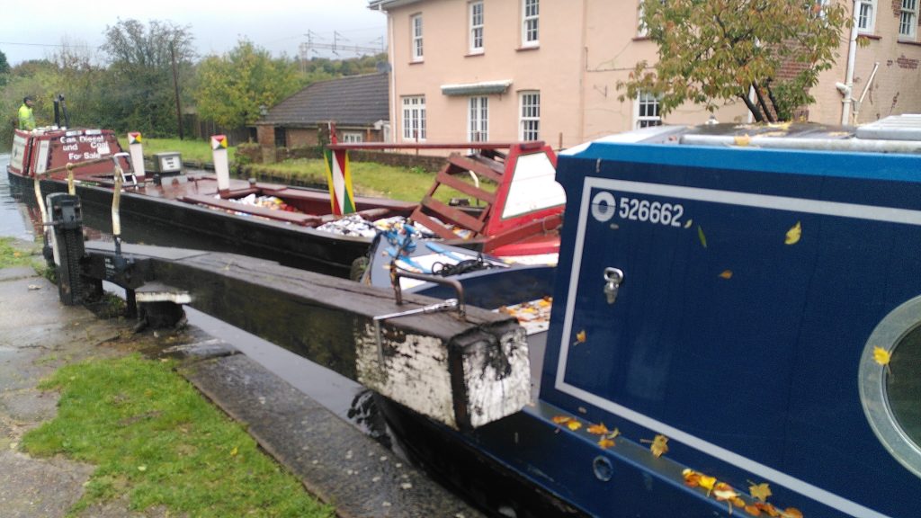 Two narrowboats pass in a lock.  The front of a modern live-aboard boat has just reached the open gate as a traditional narrowboat enters on the other side.  The traditional boat has sacks of coal and a diesel pump in front of the small cabin at the back.