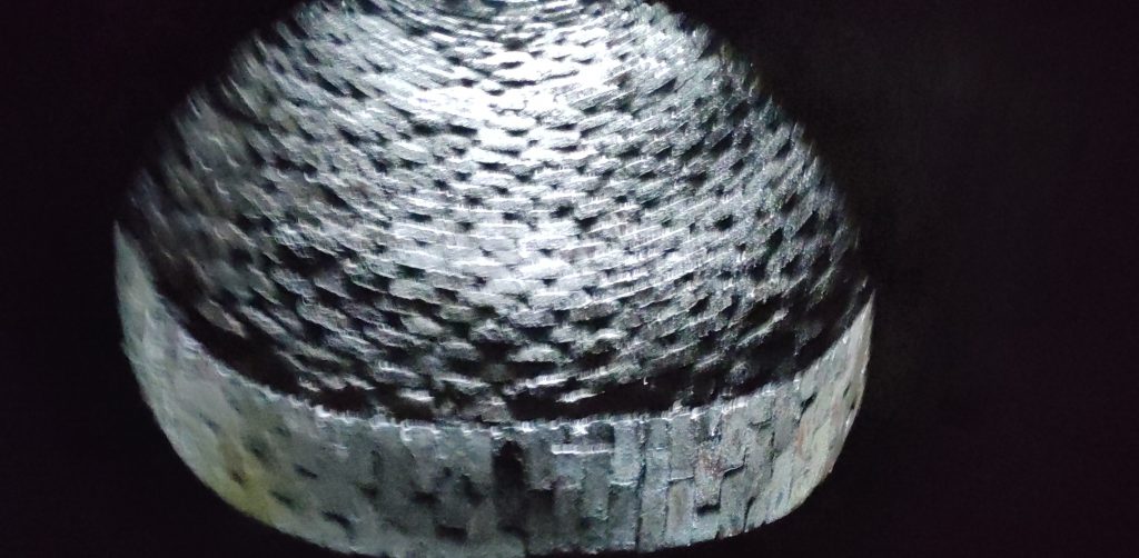 Tunnel ventilation shaft.  Looking up from the bottom of a ventilation shaft.  A circular hole in the brickwork of the tunnel roof gives way to a brick lined shaft.  The bricks lining the shaft look more like weaving.
