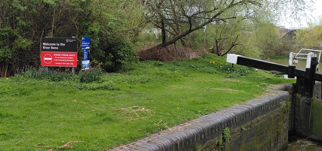 Red board.  A red sign is prominently displayed at the side of an empty canal lock.  The grass at the side of the lock is neatly trimmed.