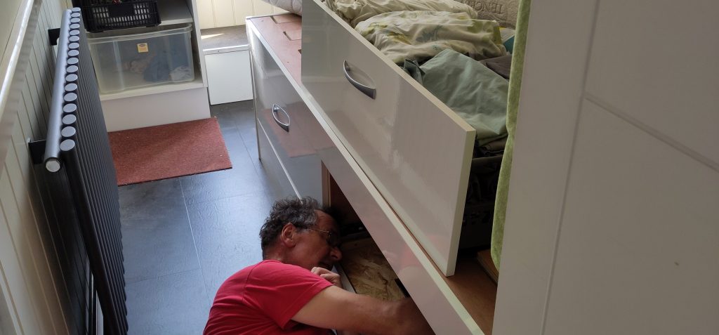Removing sensor.  A man is lying on his side with his arms under a high-sided bed.  One of the large under-bed drawers has been lifted up on to the bed allowing access underneath.