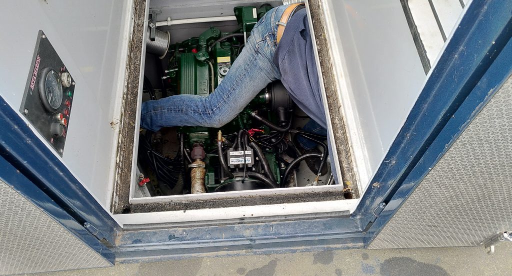 Engineer on board.  The cover is off the engine bay.   The leg of an engineer is astride the engine, but the rest of his body is largely obscured as he heads underneath the deck.