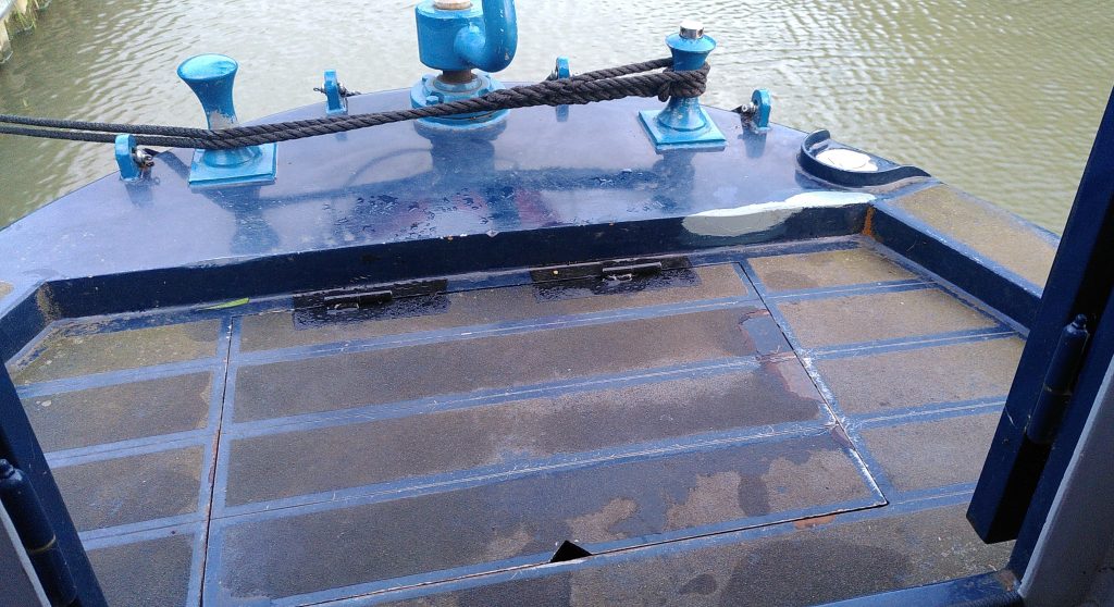 Weed hatch cover.  The stern of a narrowboat has a small trap door like cover with a small notch to allow it to be lifted.  It is a very tight fit.  The hinges at the back are painted a slightly darker colour than the surrounding metal.