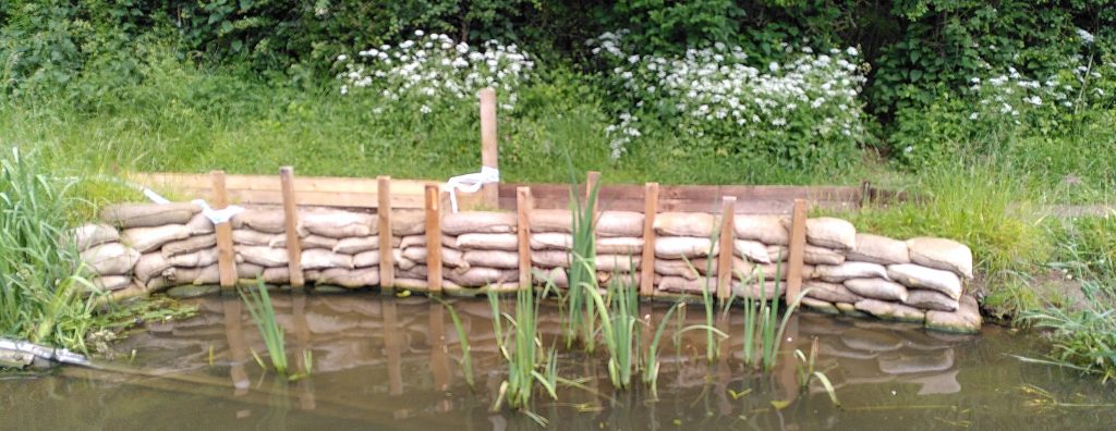 Flood damage.  A section of towpath has been temporarily shored up.  The repair has been effected with sandbags and a temporary wooden frame.