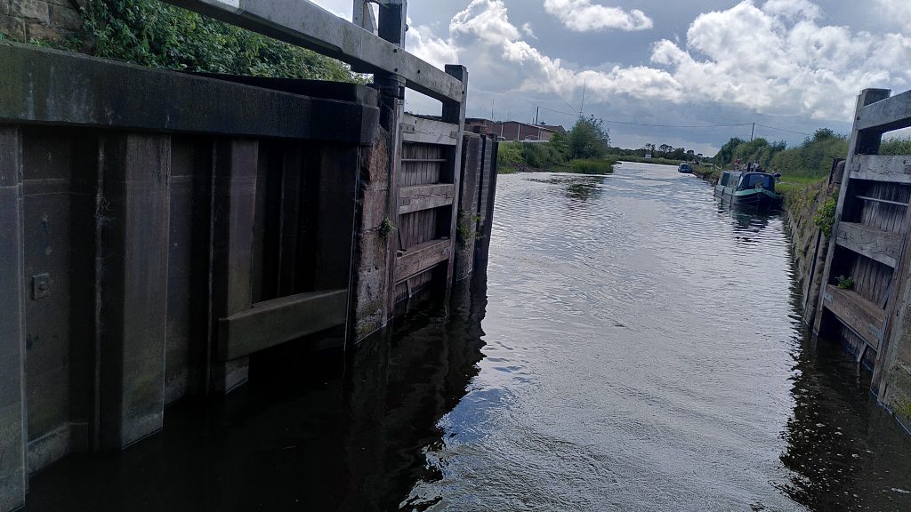 Trent flood gates.  Lock gates viewed from a boat which has just passed through.  The gates are set in to a barrier with steel piling. The closed gates are higher than any of the land visible beyond, including the towpath which is itself several feet above the current water height.