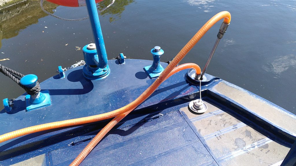 Fuel hoses. The fuel cap has been removed and placed on the rear deck of a narrowboat. Two hoses are inserted in to the fuel filler. The return hose is placed much higher than the extraction hose.
