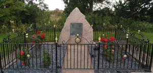 Trent Chase Memorial. A memorial stone made of Scottish granite stands in a fenced off area. Red roses bloom inside the fence. A bronze plaque lists the names of those who died on a military exercise in 1975.
